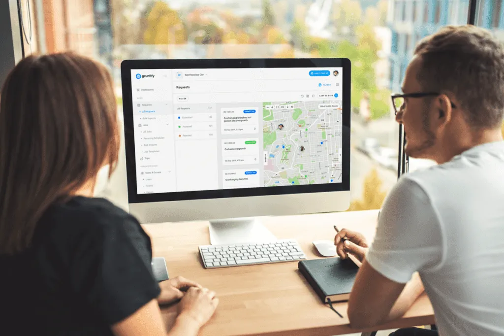 Two colleagues reviewing the Gruntify requests dashboard and map on a desktop monitor