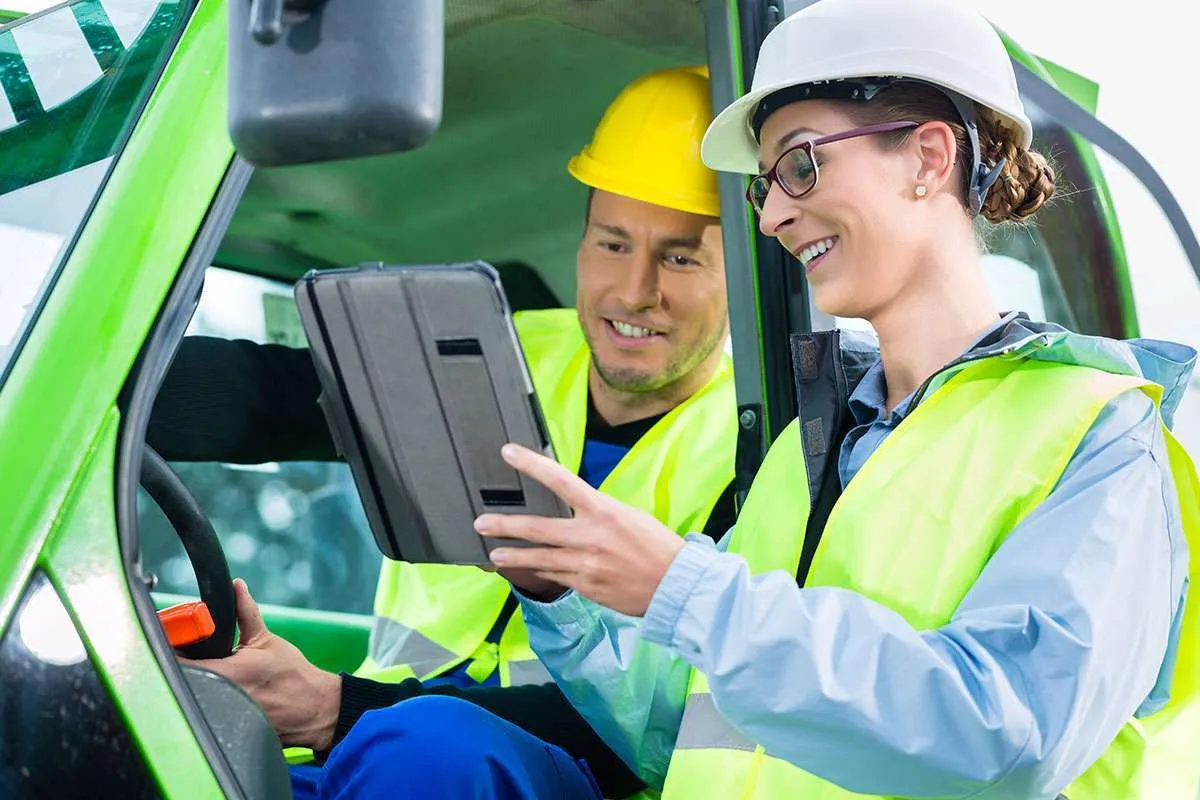 Two workers in hard hats reviewing a tablet inside a vehicle cab