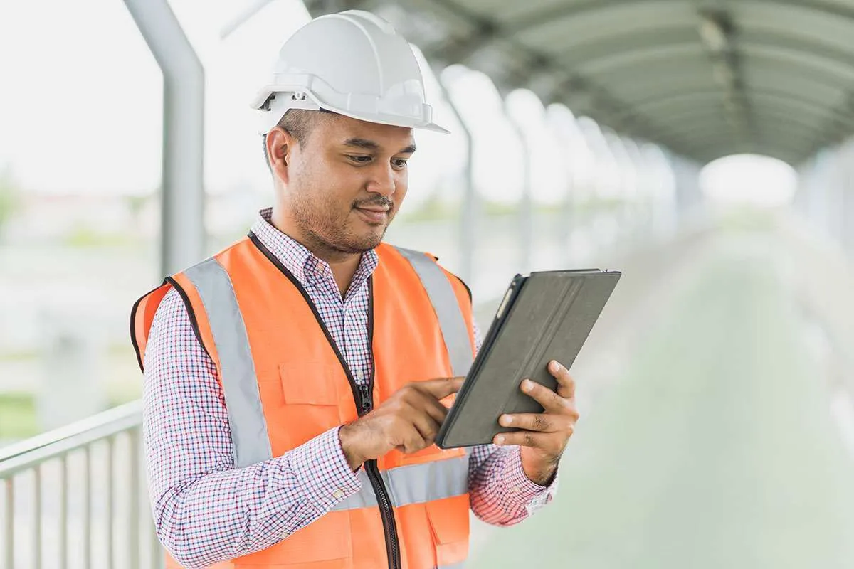 Field service worker in a high-vis vest reviewing a tablet on site