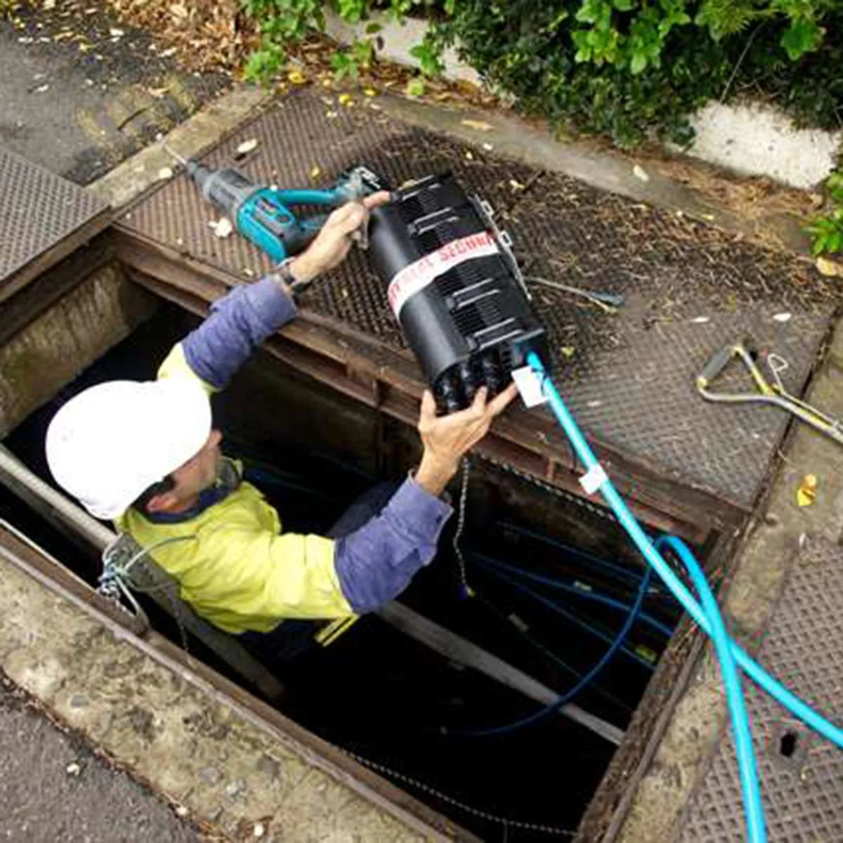 A technician replacing parts inside a telecommunications pit