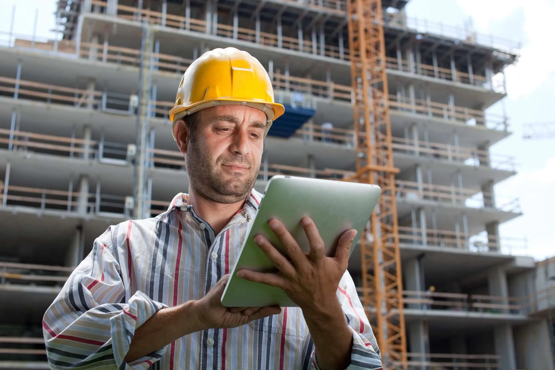 A worker in a hard hat using a tablet on a construction site