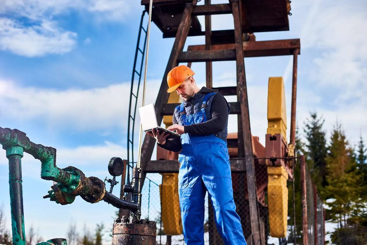 Male oil and gas worker working on a laptop while in the field.