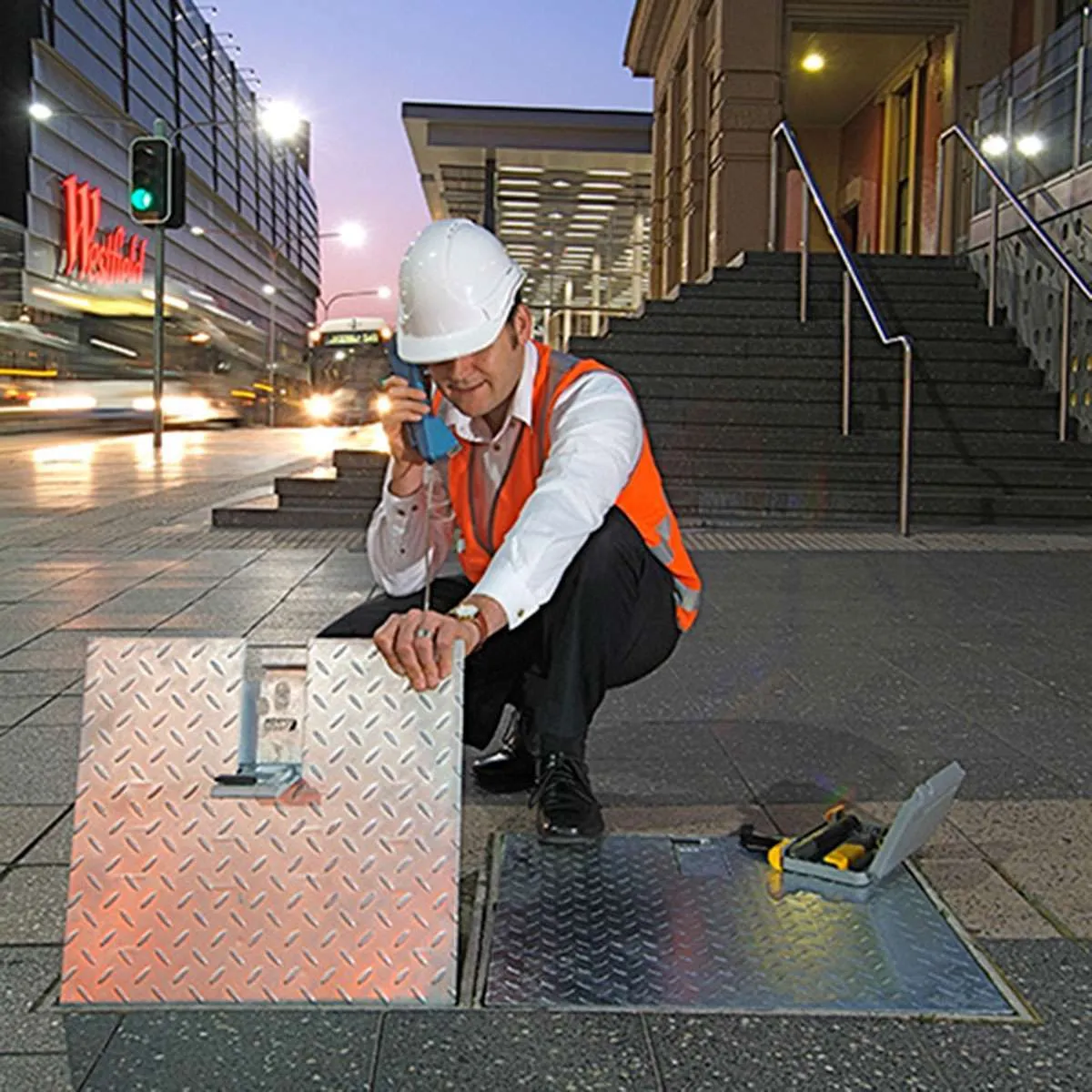 A technician inspecting a telecommunications pit on a street