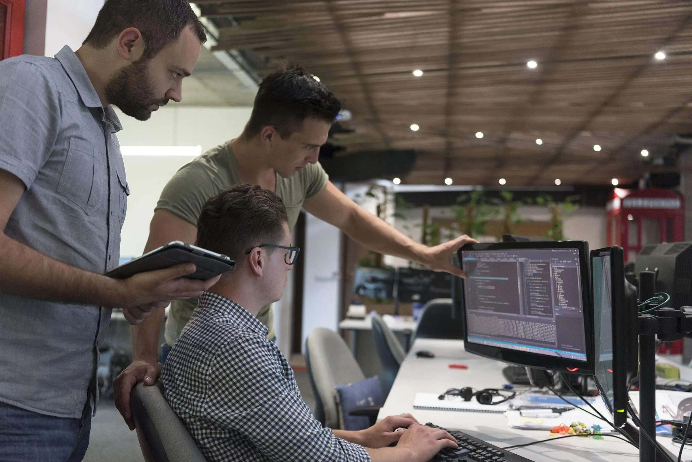 Three developers gathered around a colleague's desk reviewing code on a monitor