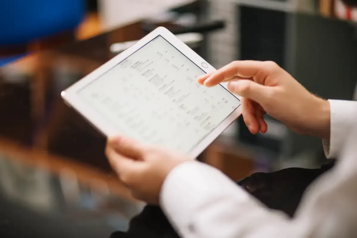 Close-up of a person’s hands scrolling through rows of data on a tablet