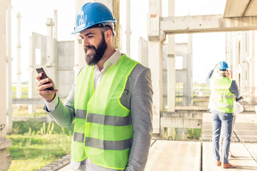 man wearing high vis hard hat using mobile app on construction site