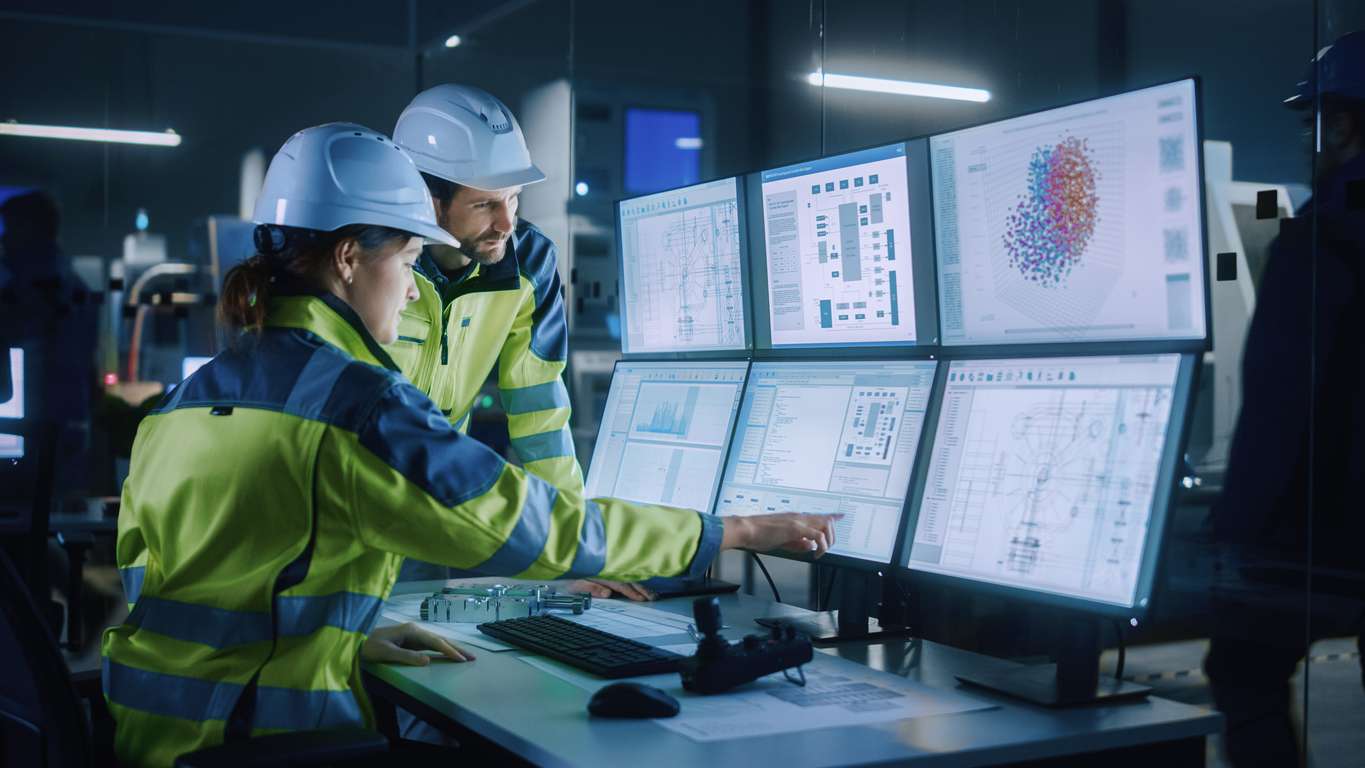 Engineers in a control room looking at computer screens showing enterprise asset management software.