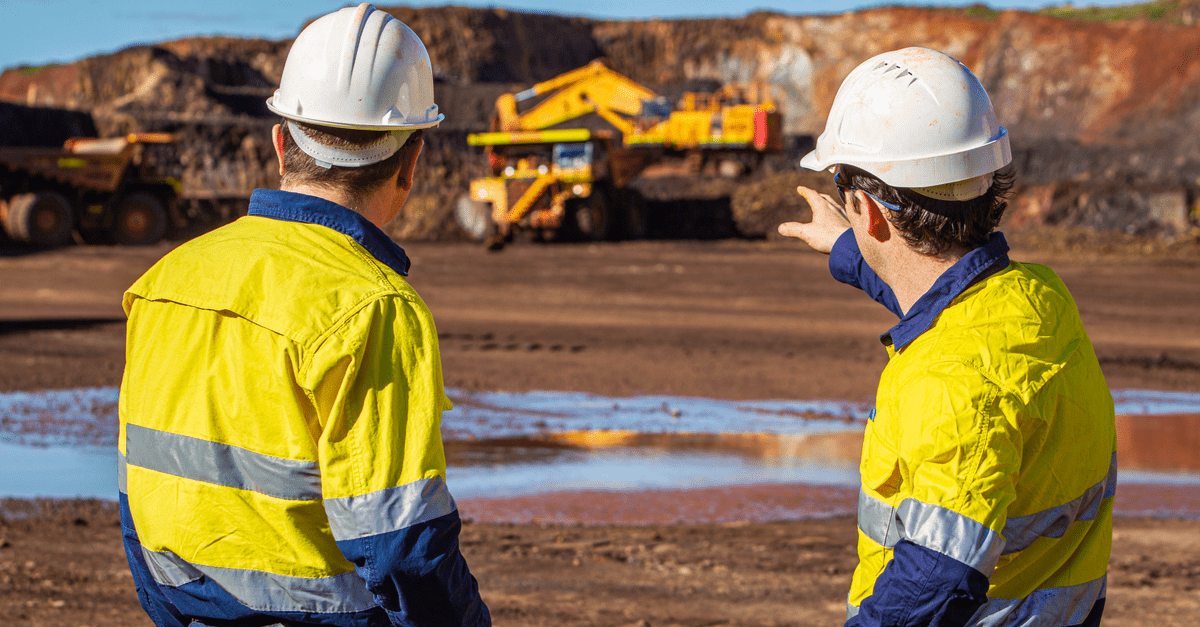 two mining engineers assessing mining work with excavator and dump truck in background