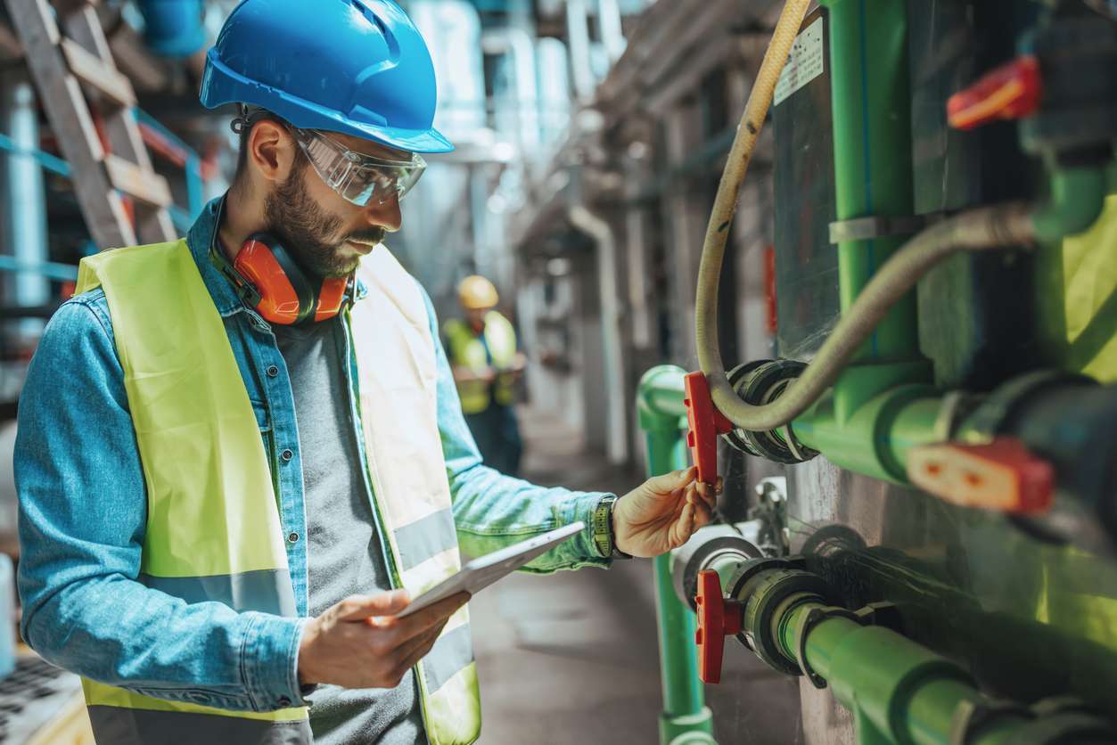 Male field service technician checking pipe system while using field service management software.